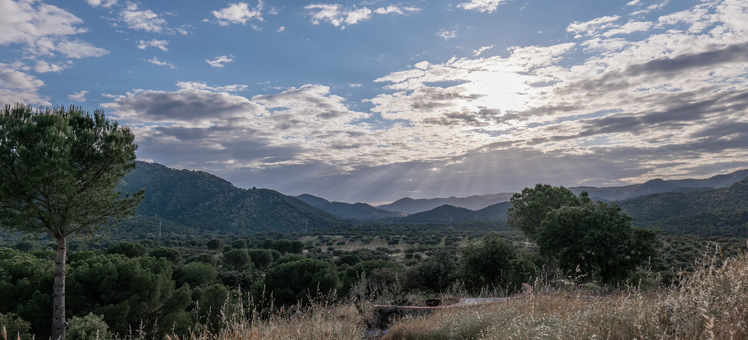 Sun breaking over the layered ridgelines of the Sierra de Andújar, oak-dotted country below