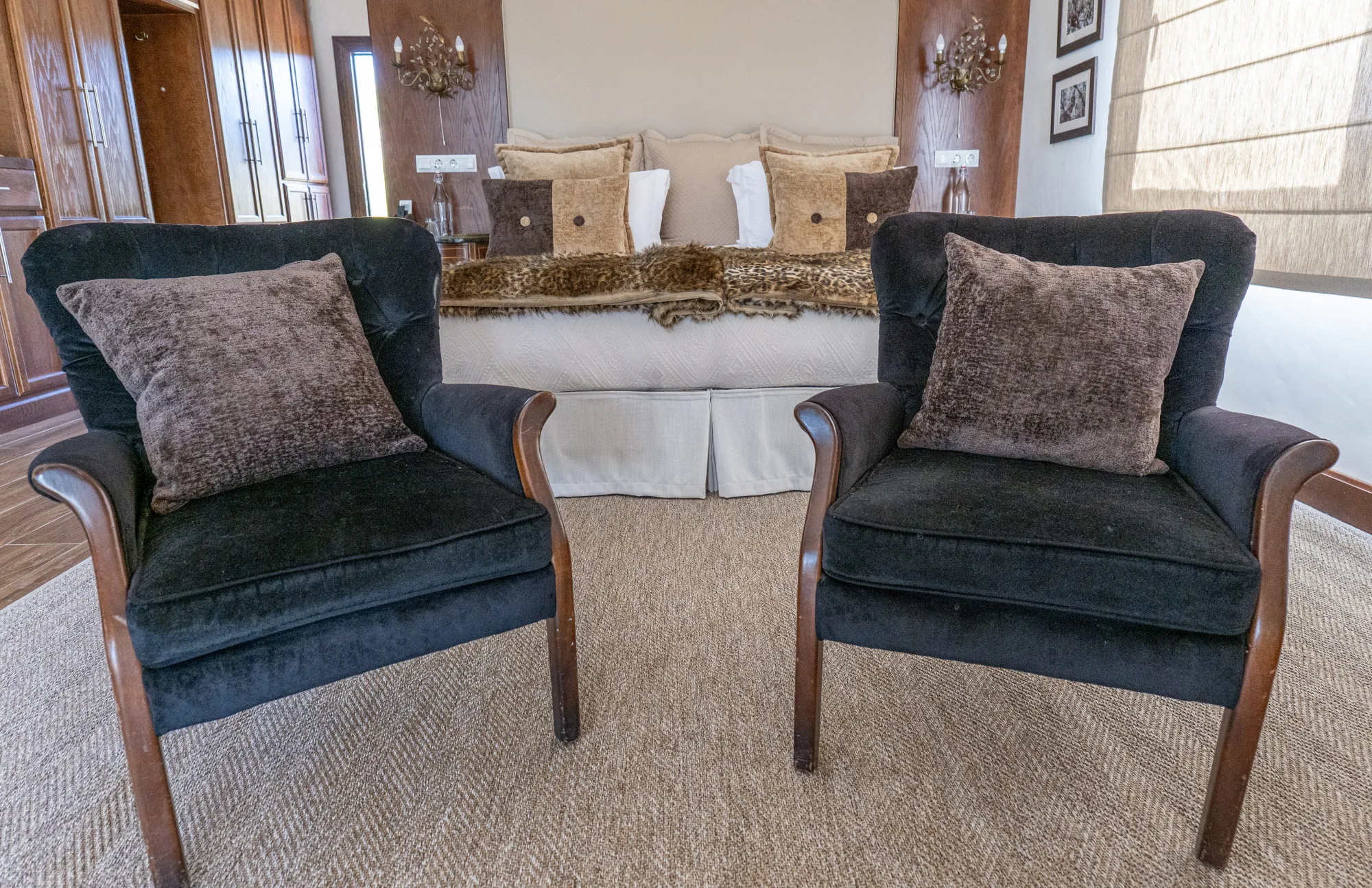 Velvet armchairs at the foot of the bed, morning light on the rug