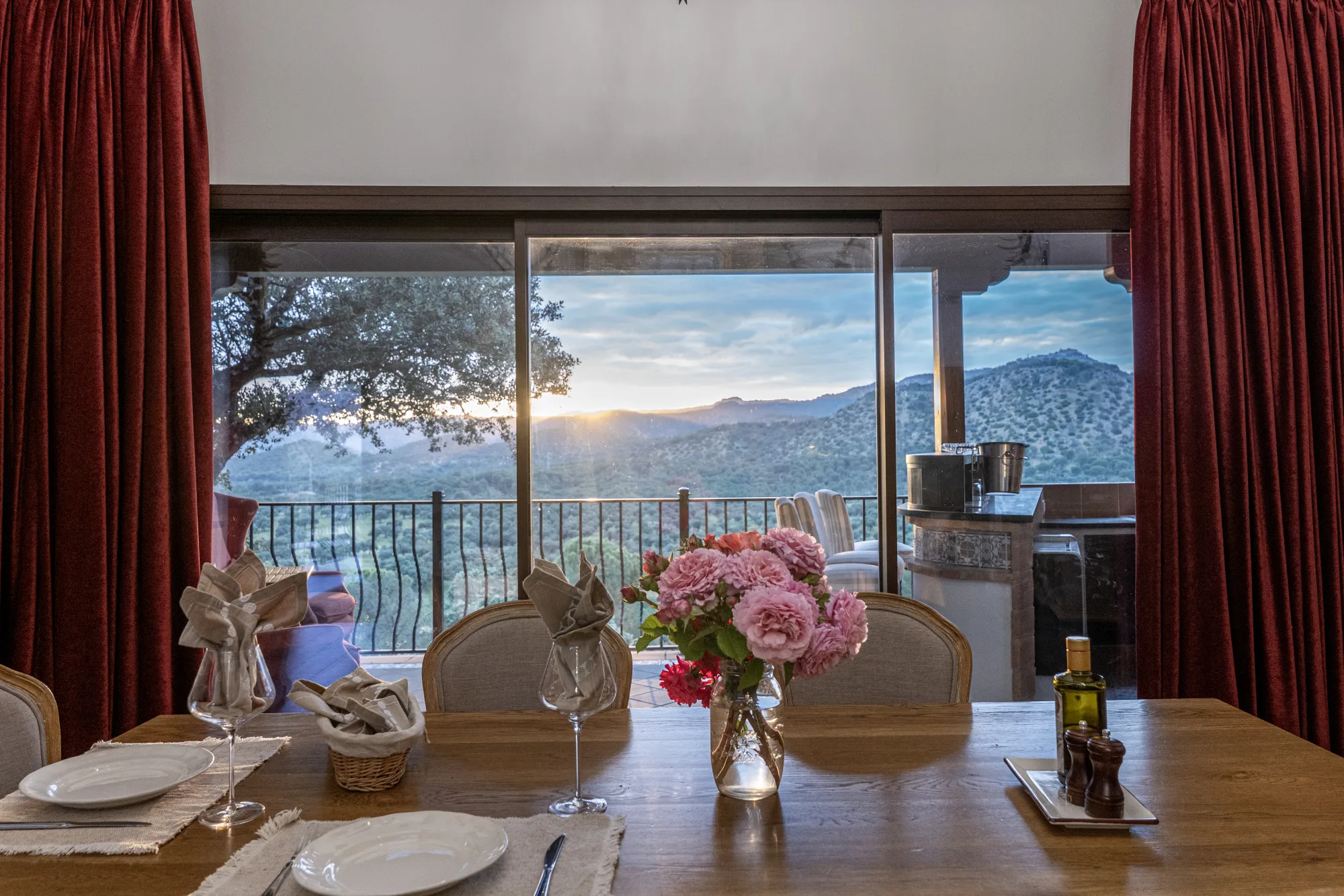 The dining table set at golden hour, mountain view through the doors