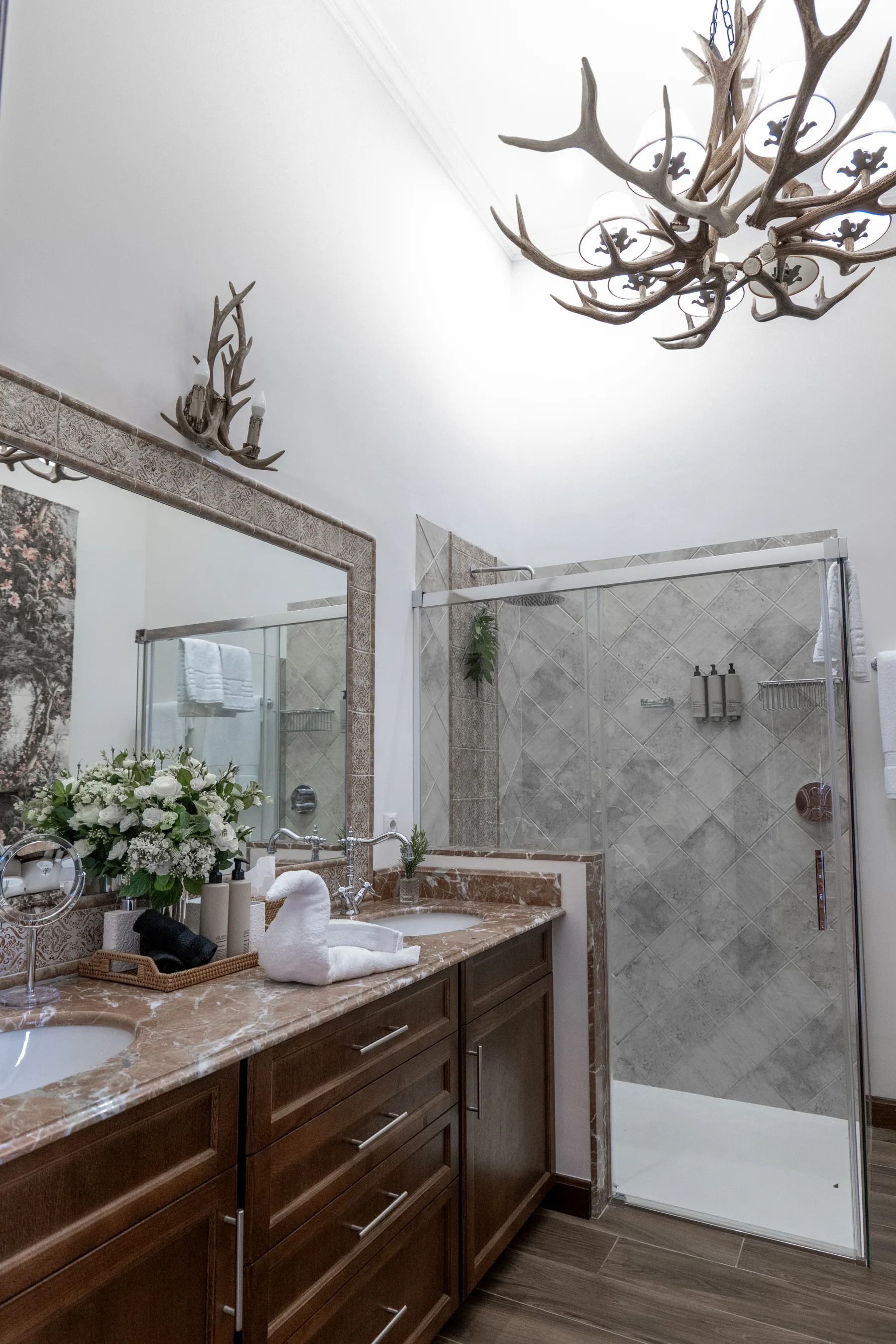 A marble vanity beneath an antler chandelier, the shower beyond