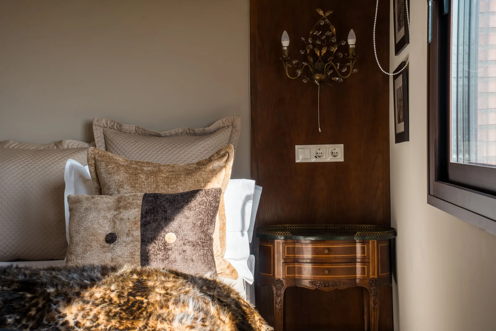 Velvet cushions and a wrought-iron sconce beside an antique commode