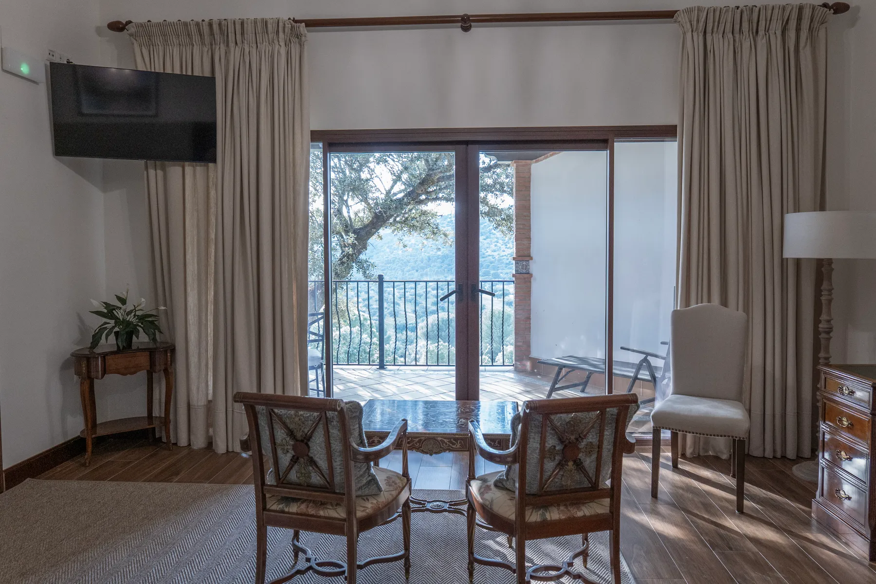 A lodge bedroom with glass doors opening onto a terrace, mountains beyond the trees