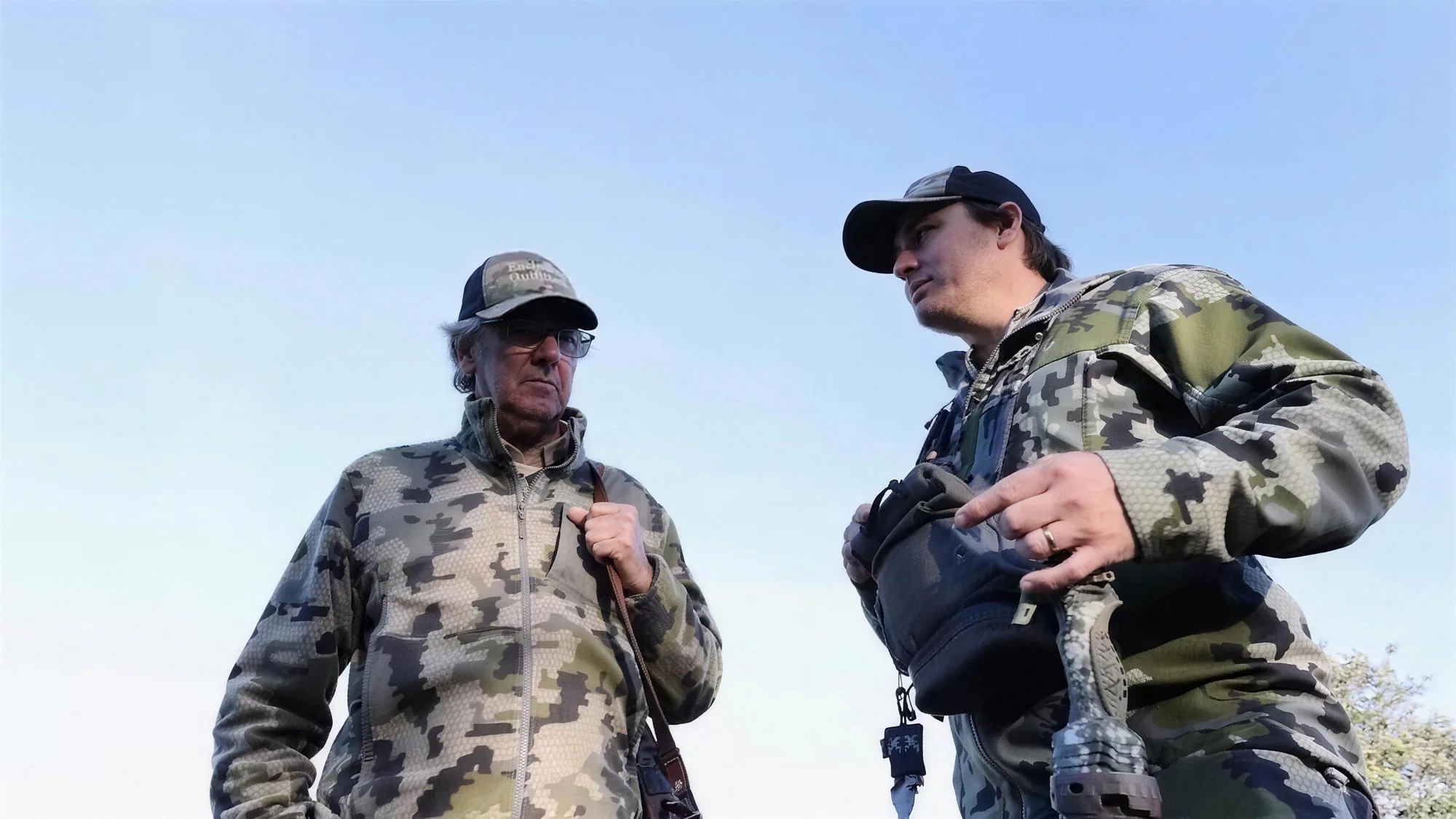 Guide and hunter pausing mid-stalk to plan the approach, binoculars at the chest